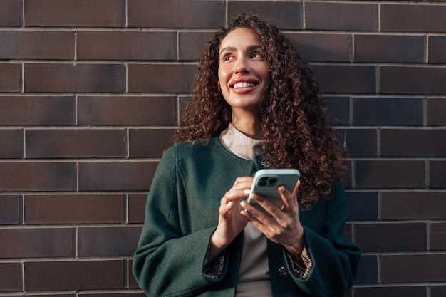 Beautiful young woman in green coat using her cellphone in the city