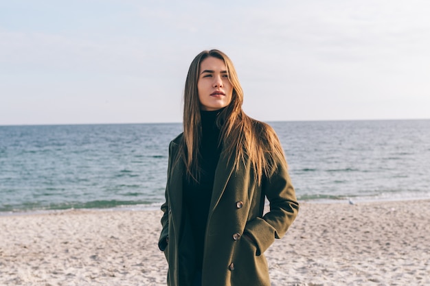 Beautiful young woman in a green coat walking along the coast