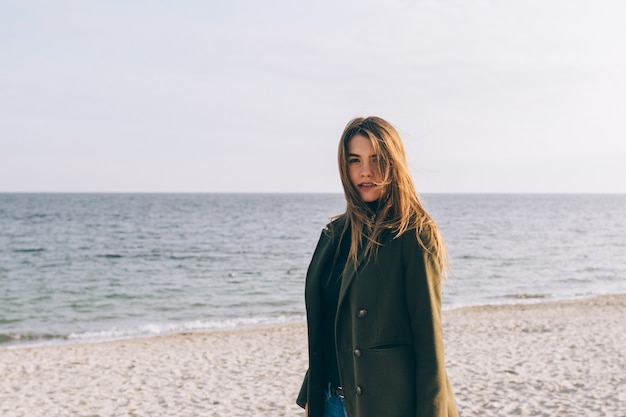 Beautiful young woman in a green coat walking along the coast