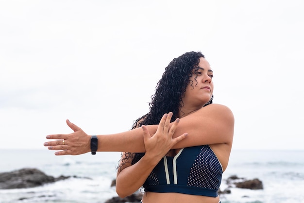 Beautiful young woman in gym clothes doing stretches on the beach sand