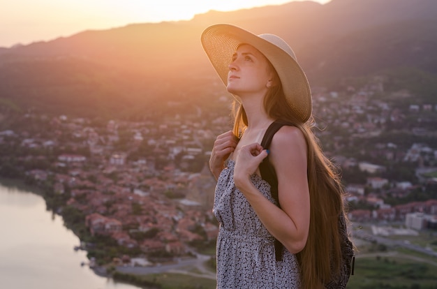 Beautiful young woman in hat on the city panorama of sunset. side view