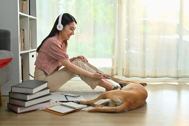 Beautiful young woman in headphone playing with dog having good time together at home Human friendship and relations