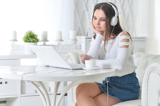 Beautiful young woman in headphones using laptop at home