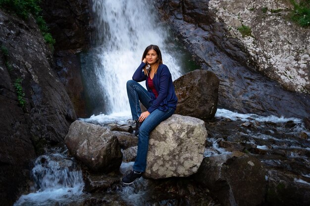 Beautiful young woman hiker sitting near waterfall