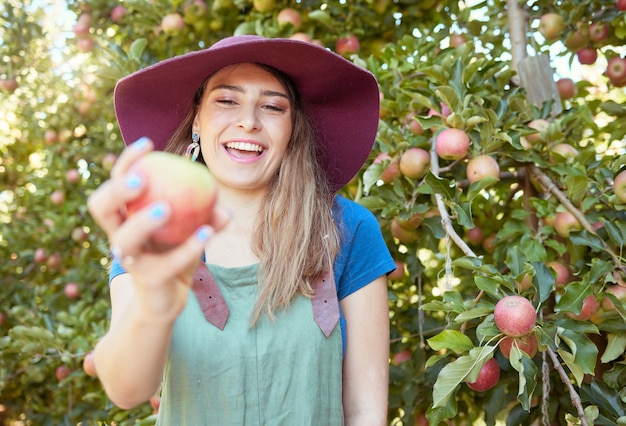 Beautiful young woman holding an apple on a farm Happy lady picking apples in an orchard Fresh fruit produce growing in a field on farmland The agricultural industry produces in harvest season