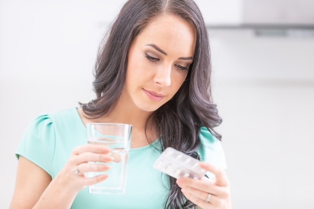 Beautiful young woman holding blister pack with pills and reading medical instructions.