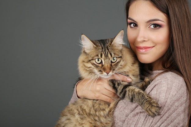 Beautiful young woman holding cat on gray background