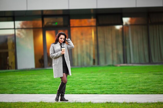 Beautiful young woman holding coffee cup and smiling while walking along the street