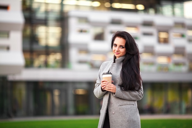 Beautiful young woman holding coffee cup and smiling while walking along the street