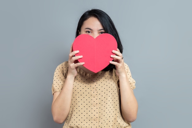 Beautiful young woman holding and covering her face with heart shaped gift box