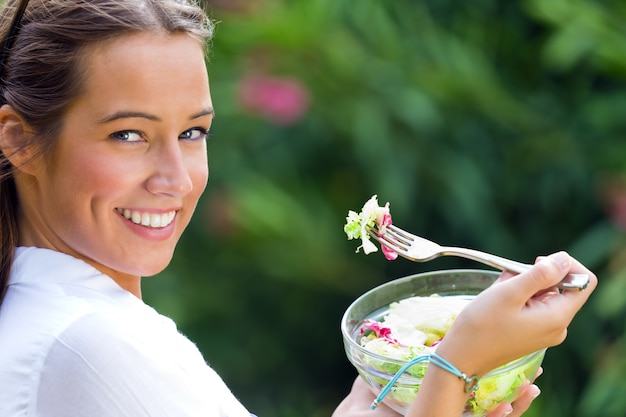 Beautiful young woman holding green salad, outdoors