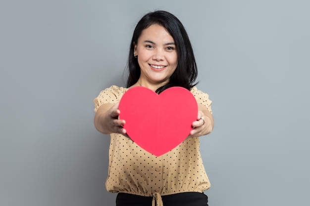 Beautiful young woman holding heart shaped gift box with both hands