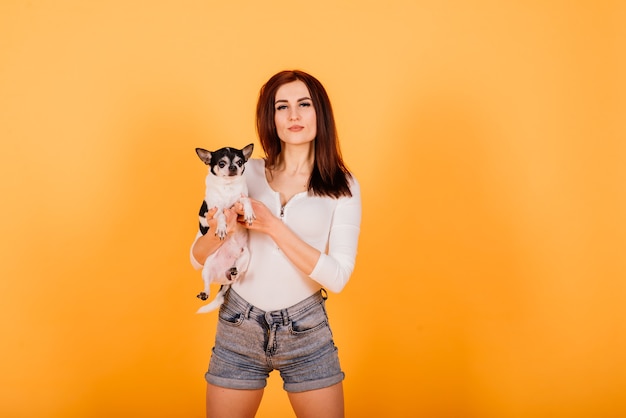 Beautiful young woman holding her dog on a yellow background.