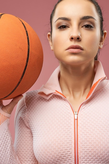 Beautiful young woman holding orange basketball ball