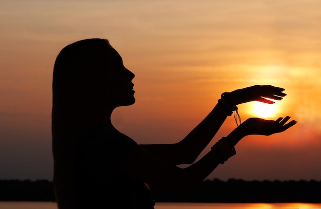 Beautiful young woman holding sun in hands on sunset silhouette