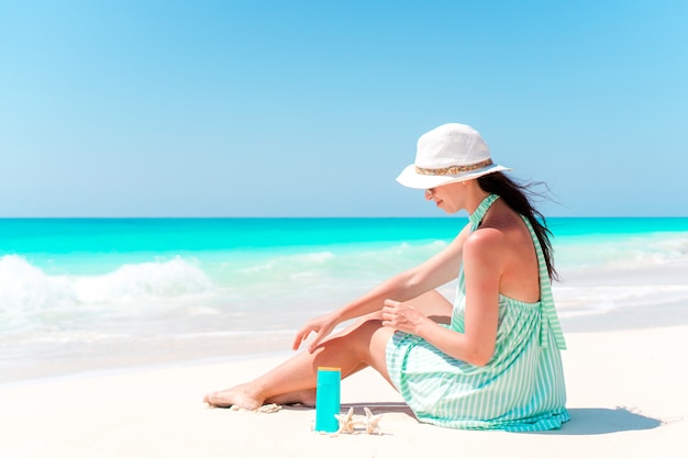 Beautiful young woman holding a suncream lying on beach