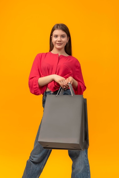 Beautiful young woman holds paper black shopping bags on yellow background Copy space Mockup Vertical frame