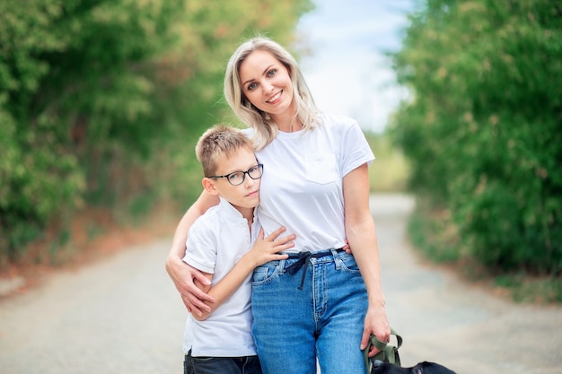 Beautiful young woman hugs her schoolboy son. A single mother walks together with a child in white T-shirts. The child wears glasses