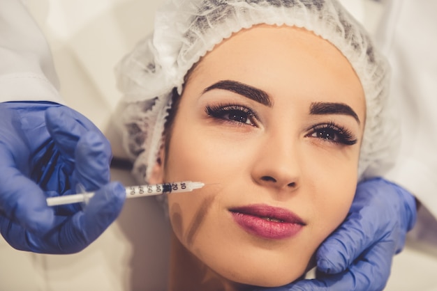 Beautiful young woman is getting an injection in face.