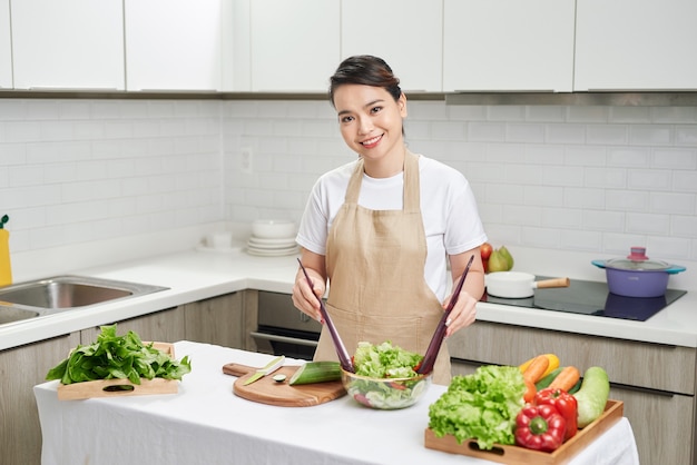 Beautiful young woman is preparing vegetable salad in the kitchen