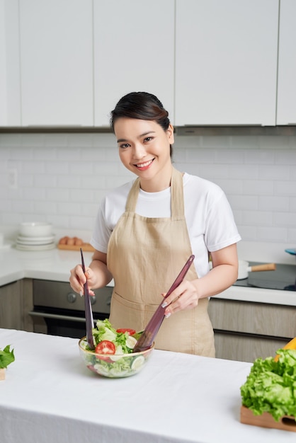 Beautiful young woman is preparing vegetable salad in the kitchen