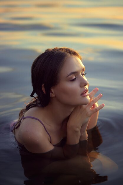 Beautiful young woman in lake water in summer dress at sunset Portrait of a romantic wet girl at sunset warm sun natural beauty of a woman