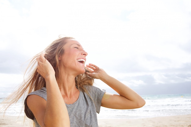 Beautiful young woman laughing at the beach with hand in hair