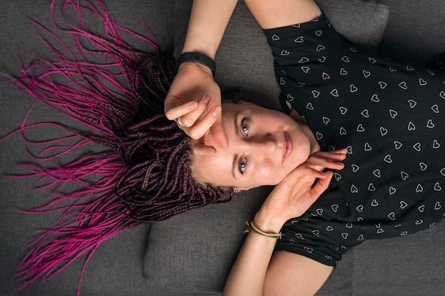 Beautiful young woman lies on couch with pink dreadlocks and tshirt with heart pattern Informal young woman