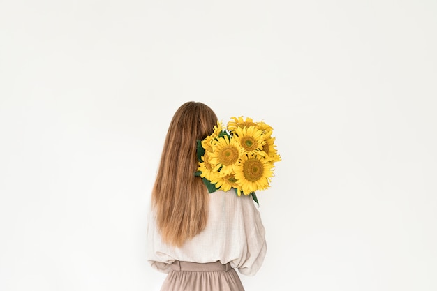 Beautiful young woman in linen dress holding sunflowers bouquet on white