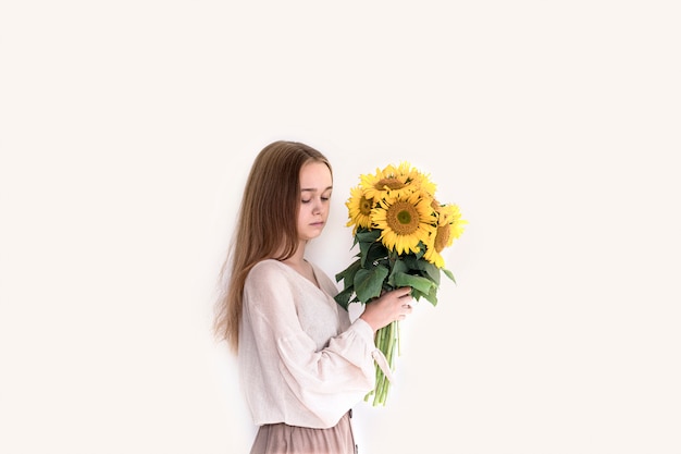 Beautiful young woman in linen dress holding sunflowers bouquet on white