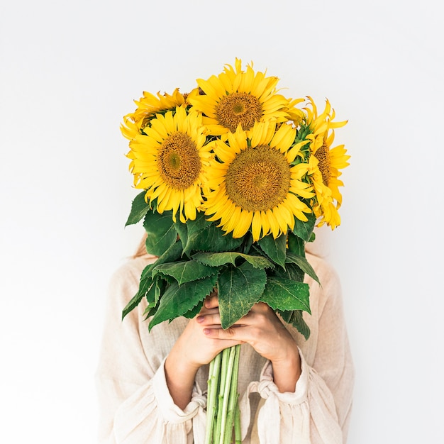 Beautiful young woman in linen dress holding sunflowers bouquet on white