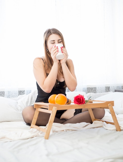 Beautiful young woman in lingerie having breakfast at morning