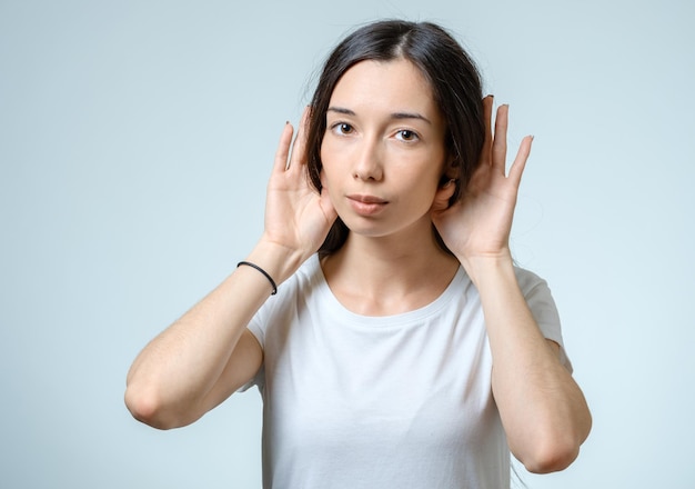 Beautiful young woman listening gossips and holding her hand near the ear