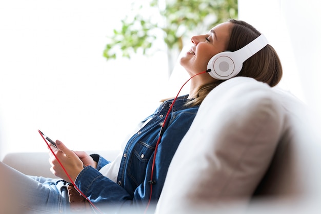 Beautiful young woman listening to music with mobile phone at home.