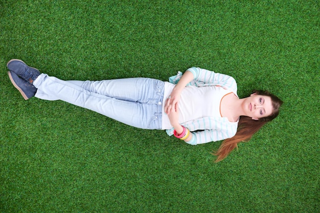 Beautiful young woman lying on the green grass