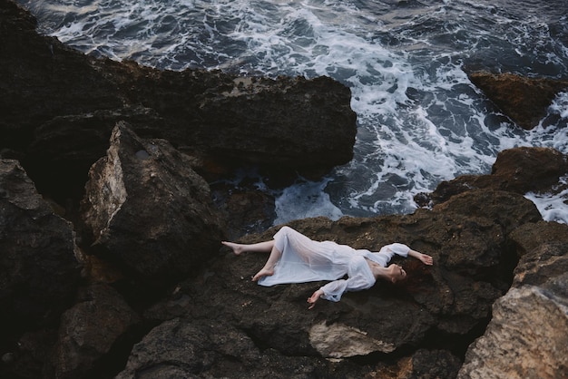 Beautiful young woman lying on her back on a rocky seashore unaltered