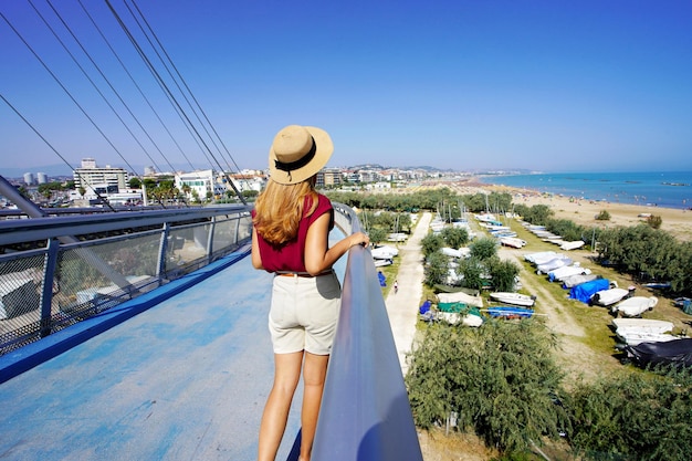 Beautiful young woman on modern bridge enjoying Pescara seascape from promenade in Abruzzo region Italy