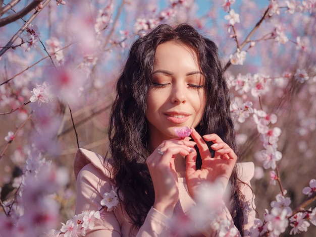 A beautiful young woman near a blooming spring cherry blossom tree. The idea and concept of renewal, self-care and happiness