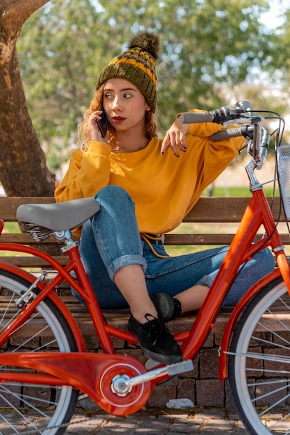 Beautiful young woman outdoors in park with bicycle beautiful spring day using mobil phone