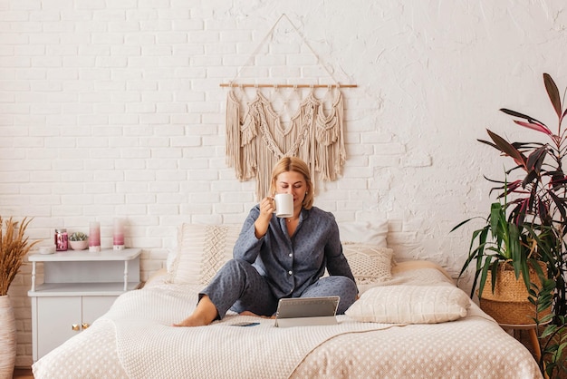 Beautiful young woman in pajamas, working on a laptop in bed, talking on the phone. Online shopping.