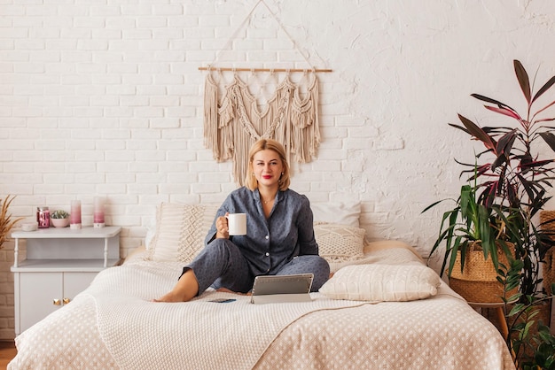 Beautiful young woman in pajamas working on a laptop in bed talking on the phone Online shopping