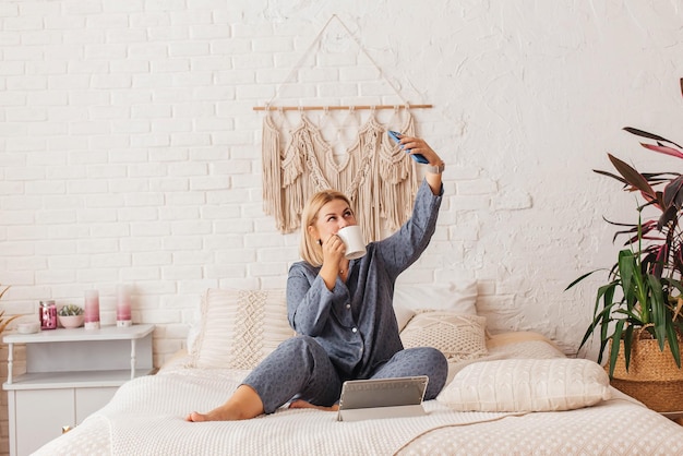 Beautiful young woman in pajamas working on a laptop in bed talking on the phone Online shopping