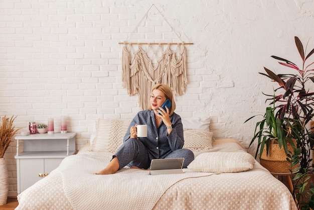 Beautiful young woman in pajamas working on a laptop in bed talking on the phone Online shopping