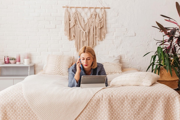 Beautiful young woman in pajamas working on a laptop in bed talking on the phone Online shopping