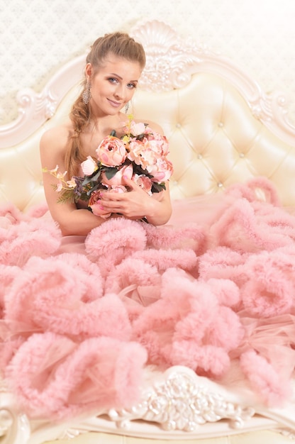 Beautiful young woman in pink dress sitting on bed