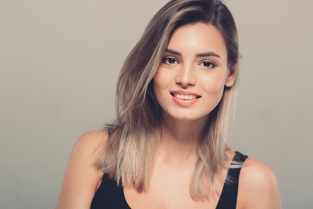 Beautiful young woman portrait in black shirt smiling posing attractive blond. Studio shot. Gray background.