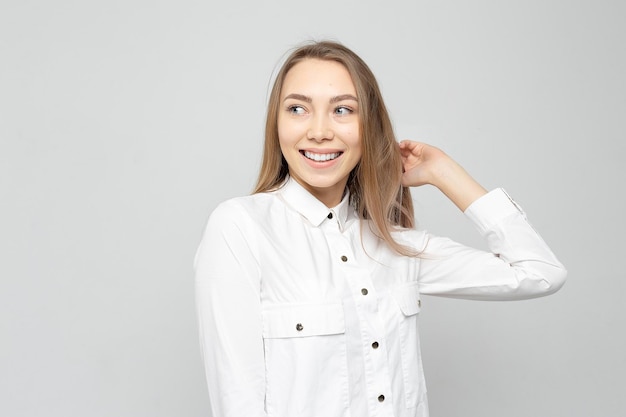 Beautiful young woman portrait Portrait of a beautiful smiling blonde in white shirt on a whitegray woman straightens her hair or holds her head