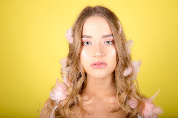 Beautiful young woman posing isolated over yellow wall background with feather