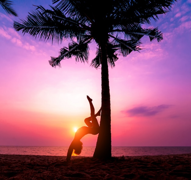 Beautiful young woman practic yoga at the beach. Early morning exercise. Sunrise