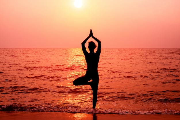 Beautiful young woman practices yoga at the beach. Early morning exercise